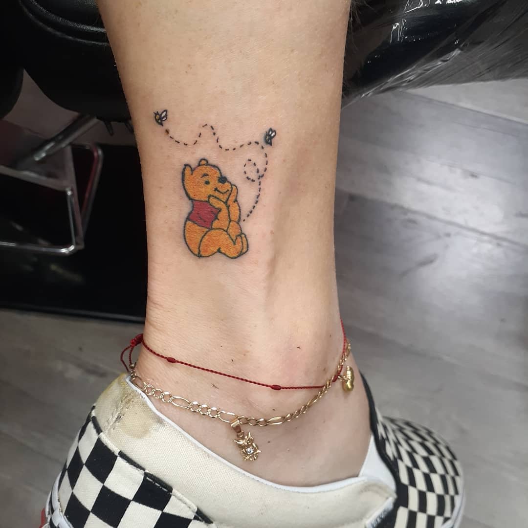 Winnie the Pooh tattoo on ankle featuring bees and dotted flight paths around him